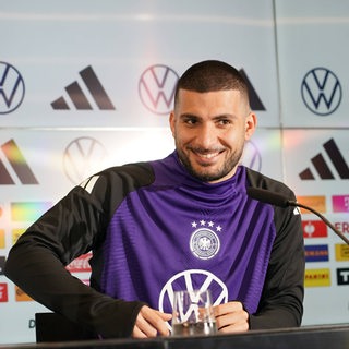 Deniz Undav grinst auf dem Podium bei einer DFB-Pressekonferenz.